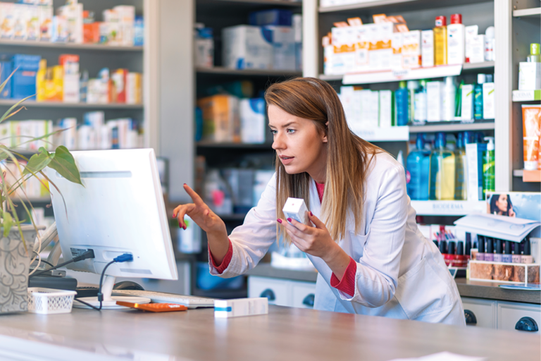 Female pharmacist holding pill bottle looking closely at computer screen