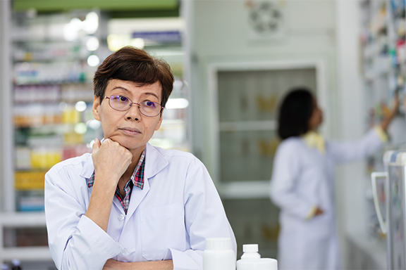 Female pharmacist leaning on counter looking tired