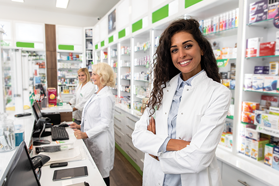 Smiling female pharmacist looking at camera with two coworkers in the background