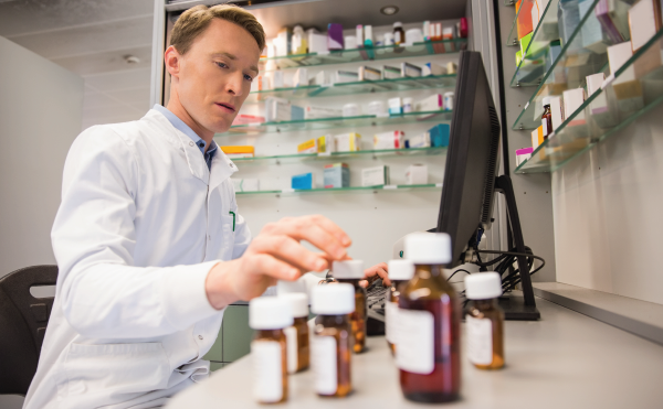 Male pharmacists sitting in front of a computer looking at a row of medications on the desk