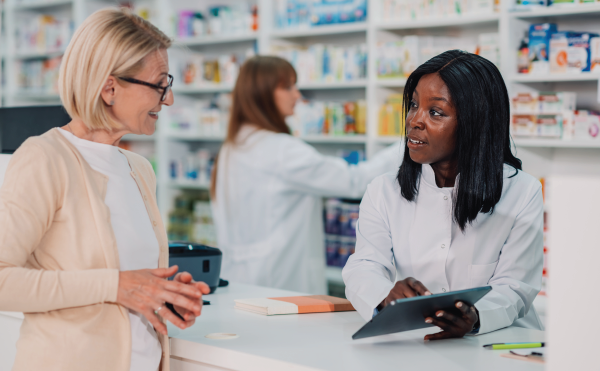 Pharmacists speaking to a patient at the counter while another pharmacist works in the background.