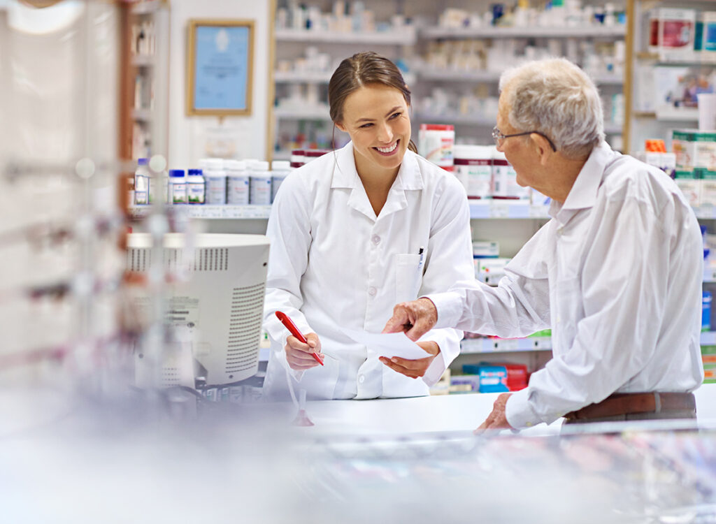 Female pharmacist at counter talking to elderly male patient