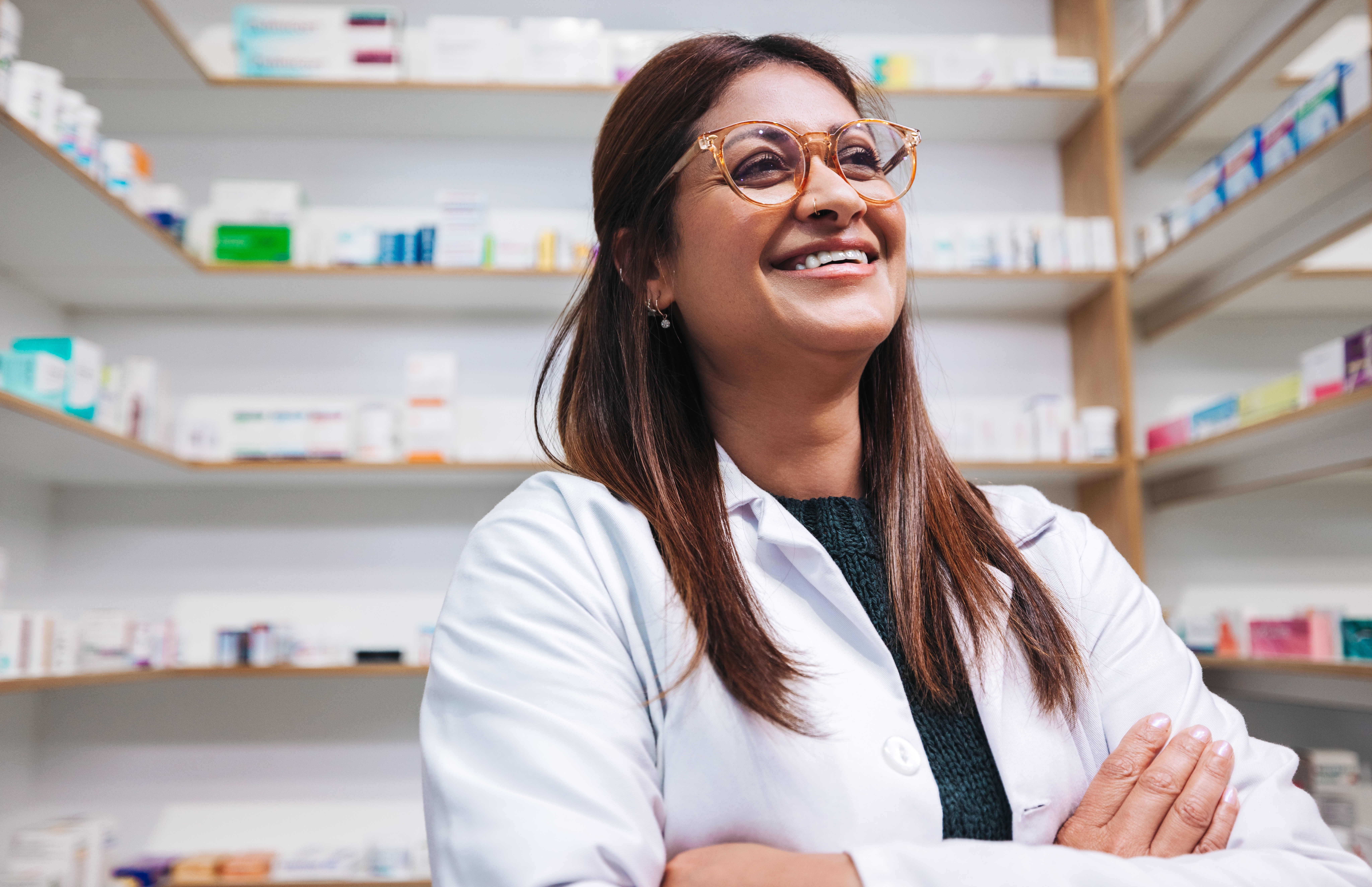 Smiling female pharmacist standing in front of shelves.
