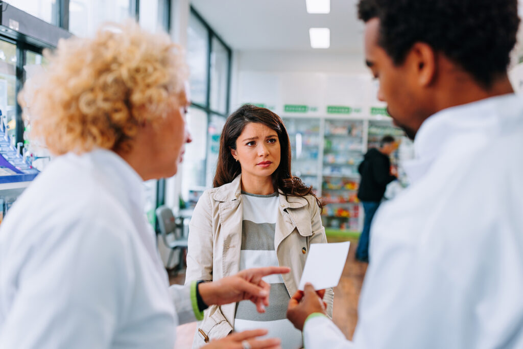 Pregnant customer at pharmacy counter with two pharmacists reviewing her medication